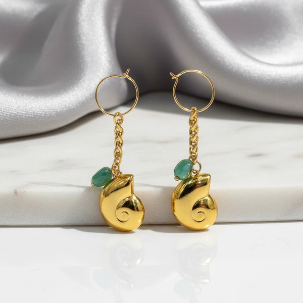 elephantina.gr gold hoop earrings with shell charms and green crystal stones on a marble surface.