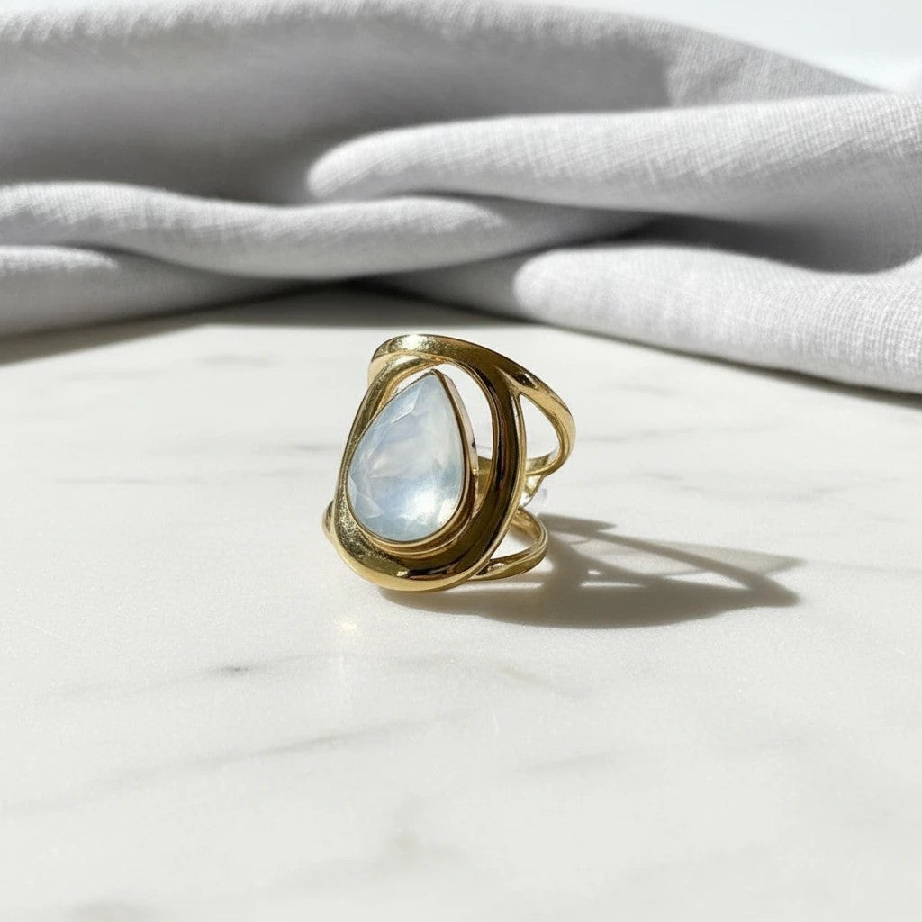 elephantina.gr gold-tone teardrop statement ring with a luminous pearlescent stone in an open-work metal frame.