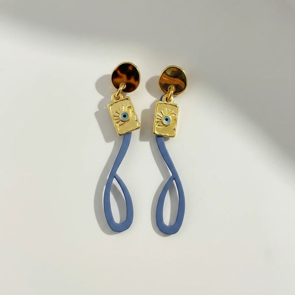 Elephantina.gr gold plated earrings with blue silicone abstract shape and evil eye detail. Modern design, 4cm length.