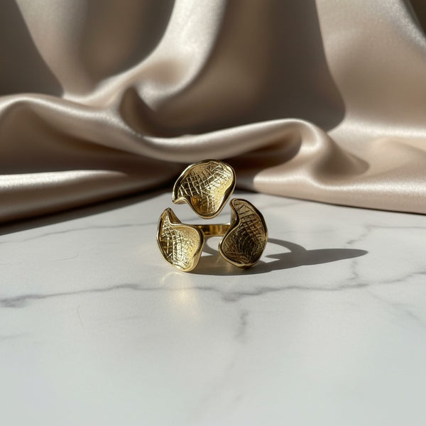 elephantina.gr gold-tone statement ring with three textured, petal-like elements on a white marble surface.