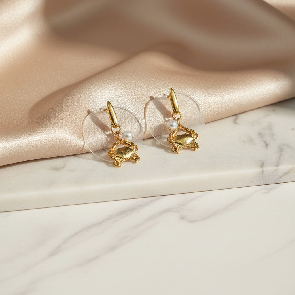 Gold-tone dangle earrings featuring detailed crab charms with a single pearl accent. elephantina.gr
