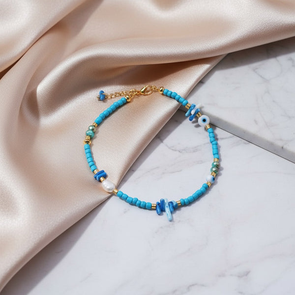 Elephantina.gr blue beaded anklet with coral, pearls, and evil eye charm. Gold accents.