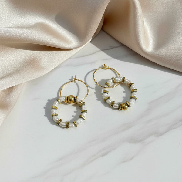 elephantina.gr handmade hoop earrings with rice pearls and gold-toned hematite beads on a marble surface.