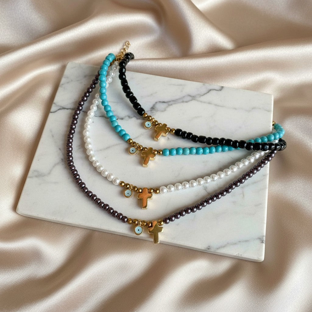 Elephantina.gr beaded necklaces with pearl, turquoise, and black beads, featuring gold crosses and blue evil eye charms.